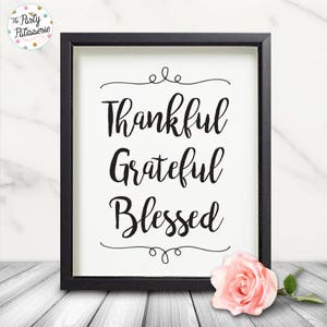 May include: Black and white framed print with the text "Thankful Grateful Blessed" in a decorative script font. The print is sitting on a white wooden surface with a pink rose.