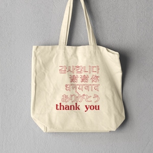 May include: A beige tote bag with red text that says "감사합니다", "谢谢", "धन्यवाद", "ありがとう", and "thank you".