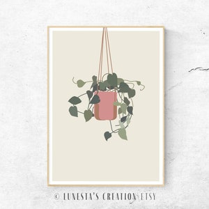 Puede incluir: Una impresión artística enmarcada que presenta una planta colgante en una maceta rosa. La planta tiene hojas verdes y está suspendida por cuerdas marrones sobre un fondo beige. La obra de arte tiene una estética minimalista y moderna.
