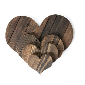May include: Three wooden hearts of varying sizes, nested together. The hearts are made of dark brown wood with a rustic finish.