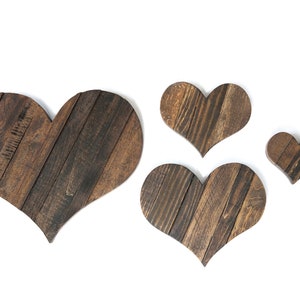May include: Four wooden hearts of varying sizes, all made of dark brown wood with a rustic finish. The hearts are arranged in a staggered pattern on a white background.