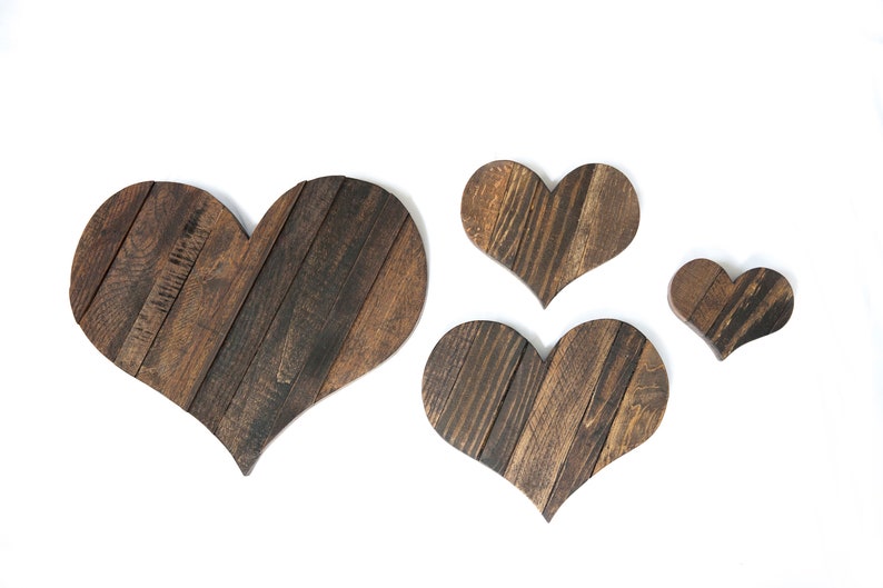 May include: Four wooden hearts of varying sizes, all made of dark brown wood with a rustic finish. The hearts are arranged in a staggered pattern on a white background.