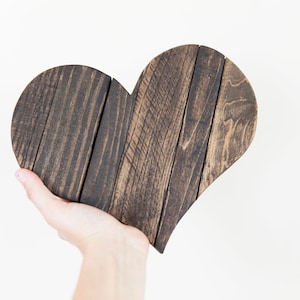 May include: A dark brown wooden heart-shaped sign, made from reclaimed wood planks, is held in a person's hand.