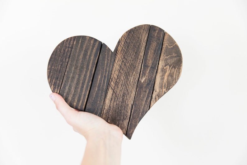 May include: A dark brown wooden heart-shaped sign, made from reclaimed wood planks, is held in a person's hand.