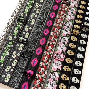 May include: Set of eight black elastic hair ties with various Halloween-themed prints. The prints include green eyes, pink lips, red and white flowers, pink and white skulls, and gold and silver skulls.