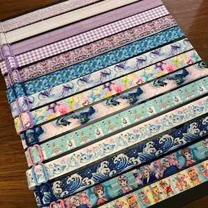 May include: A collection of 14 colorful hair ties with various patterns, including a purple gingham, a blue and white wave pattern, and a pink and blue narwhal pattern.