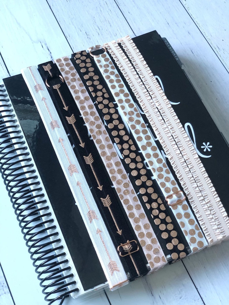 Puede incluir: Un conjunto de ocho bandas el&aacute;sticas para libros de color negro y oro rosa con diferentes patrones, que incluyen lunares, purpurina y flechas. Las bandas est&aacute;n dispuestas en una agenda negra con una encuadernaci&oacute;n en espiral dorada.