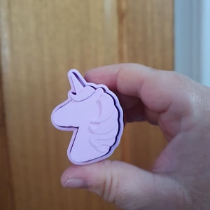 May include: A purple plastic unicorn cookie cutter. The cutter is shaped like a unicorn's head with a horn and mane.