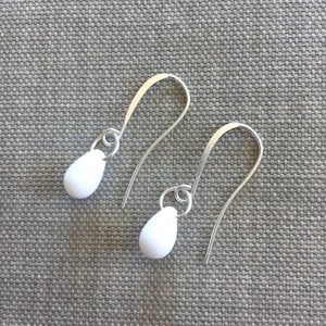 May include: A pair of silver dangle earrings with white teardrop-shaped beads.