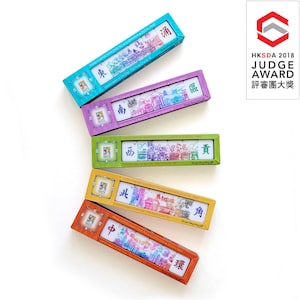 May include: Five colourful boxes of hand-carved mahjong tiles, each with a different city landscape illustration. The boxes are in shades of blue, purple, green, yellow, and orange. The text "HKSDA 2018 JUDGE AWARD" is visible.