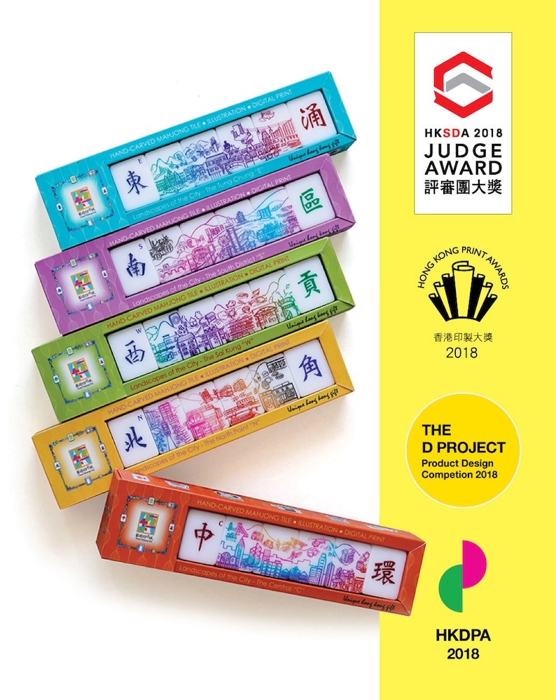 Peut inclure: Plusieurs bo&icirc;tes color&eacute;es de tuiles de Mahjong sculpt&eacute;es &agrave; la main. Chaque bo&icirc;te pr&eacute;sente une couleur diff&eacute;rente et contient des tuiles avec des illustrations de villes et des caract&egrave;res chinois. Les bo&icirc;tes sont &eacute;tiquet&eacute;es avec le texte "HAND-CARVED MAHJONG TILE ILLUSTRATION DIGITAL PRINT."