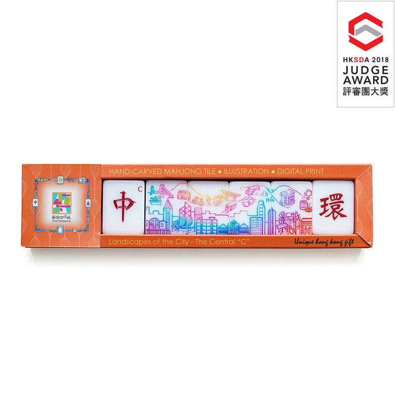 Peut inclure: Un coffret de tuiles de mahjong sculpt&eacute;es &agrave; la main. Les tuiles pr&eacute;sentent des illustrations color&eacute;es de paysages urbains, avec le texte "Landscapes of the City - The Central 'C'" et des caract&egrave;res chinois. La bo&icirc;te est orange avec le texte "Unique hong kong gift".