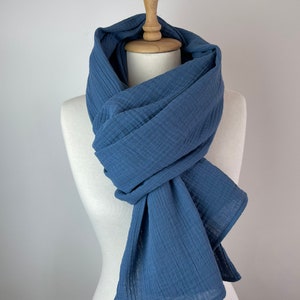 May include: A blue scarf displayed on a mannequin. The scarf, made from textured fabric, is a solid blue. It's wrapped around the mannequin's neck and drapes down. The mannequin is white, with a wooden neck. The scarf's texture is clearly visible.