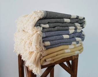 Puede incluir: Una pila de cuatro toallas rayadas con flecos. Las toallas son en tonos de negro, azul y amarillo.