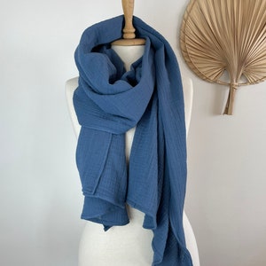May include: A blue scarf displayed on a mannequin. The scarf is made of a soft, textured material and is draped around the mannequin's neck and shoulders. The scarf's colour is a muted blue, and it has a flowing, lightweight appearance.