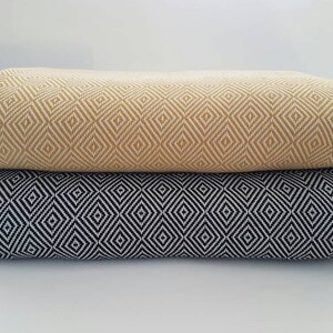 May include: Two folded textiles, one mustard yellow and one black, each with a repeating diamond pattern. The fabrics are stacked on top of each other, showcasing the detailed weave and color contrast. The background is plain white.