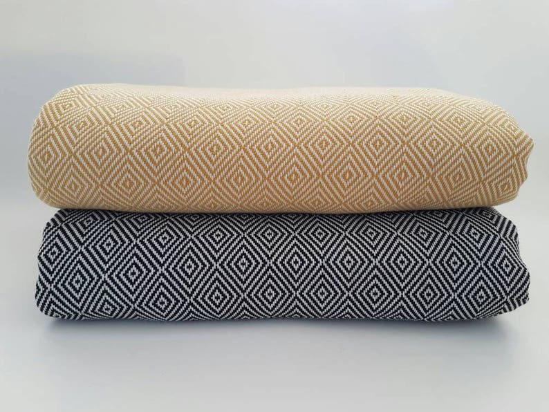 May include: Two folded textiles, one mustard yellow and one black, each with a repeating diamond pattern. The fabrics are stacked on top of each other, showcasing the detailed weave and color contrast. The background is plain white.