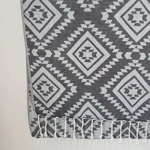 May include: A gray and white patterned textile with a geometric design. The pattern features diamond shapes and triangles. The bottom edge has white fringe.