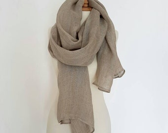 May include: A light brown linen scarf draped over a white mannequin. The scarf is made of a soft, lightweight fabric and has a simple, elegant design.