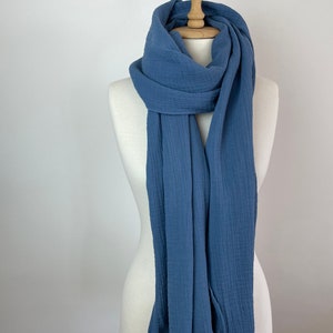 May include: A blue scarf displayed on a mannequin. The scarf is made of a soft, textured material and has a flowing, lightweight appearance. The scarf is a solid colour and appears to be a versatile accessory.