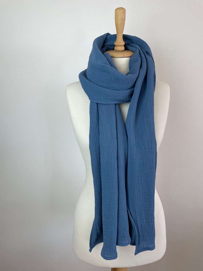 May include: A blue scarf displayed on a mannequin. The scarf is made of a soft, textured material and has a flowing, lightweight appearance. The scarf is a solid colour and appears to be a versatile accessory.