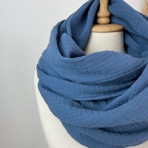 May include: A blue infinity scarf made from a soft, textured material. The scarf is displayed on a mannequin, highlighting its circular design and how it would be worn. The colour is a muted, dusty blue.