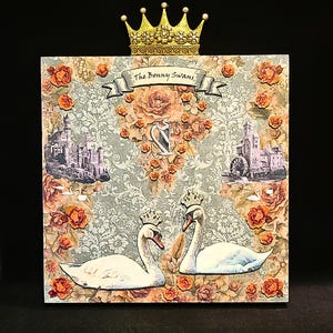 Könnte beinhalten: Eine quadratische, dekorative Holzkiste mit floralem Design und zwei weißen Schwänen. Die Kiste hat eine goldene Krone oben und den Text "The Bonny Swans" auf einem Banner.