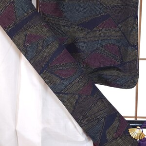 May include: Close-up of a patterned kimono with a geometric design in navy, burgundy, and gold. The kimono's interior is white, and the trim is a deep burgundy. A decorative tassel hangs from the side.