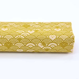 Pode incluir: Um tecido amarelo com um padrão branco de gatos estilizados e ondas. O tecido tem uma superfície texturizada.