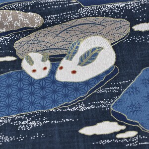 May include: Close-up of a fabric with a Japanese-inspired design. The pattern features two white rabbits with red eyes and blue and gold accents, set against a dark blue background with stylized water and cloud motifs.