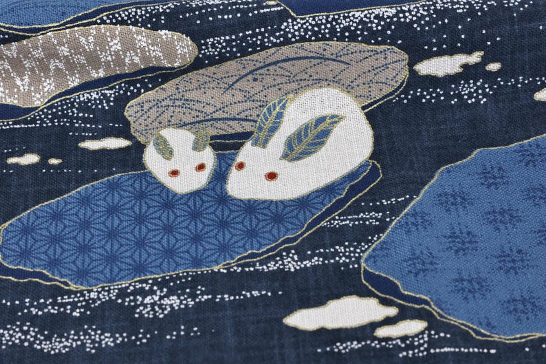 May include: Close-up of a fabric with a Japanese-inspired design. The pattern features two white rabbits with red eyes and blue and gold accents, set against a dark blue background with stylized water and cloud motifs.