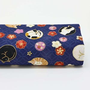 Könnte beinhalten: Gefalteter Stoff mit marineblauem Hintergrund, der ein sich wiederholendes Muster aus schlafenden Katzen, roten und rosa Blumen und weißen Blüten zeigt. Der Stoff hat ein strukturiertes Aussehen und eine japanische Ästhetik.