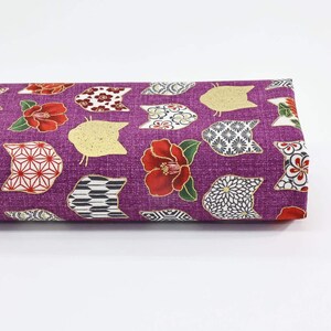 Peut inclure: Tissu violet avec un motif répété de visages de chats dorés, de fleurs rouges et de motifs géométriques.