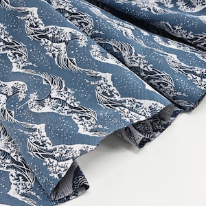 Peut inclure: Gros plan sur un tissu bleu avec un motif de vagues blanches. Le tissu est plié, révélant la texture et le design. Le motif rappelle la célèbre œuvre d'art japonaise, "La Grande Vague de Kanagawa."