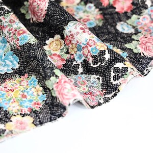 May include: Black fabric with a floral pattern in shades of pink, blue, yellow, and white. The fabric has a textured surface and is folded over.