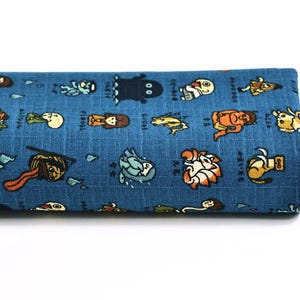 Peut inclure: Un morceau de tissu bleu plié présentant un motif répétitif de diverses créatures de dessin animé colorées et de caractères japonais. Le textile présente une texture quadrillée visible, chaque personnage étant imprimé distinctement.