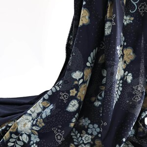 May include: Navy fabric with a floral design in white, pale blue, and gold. The fabric is draped, revealing the intricate pattern of flowers and leaves. The background is white.