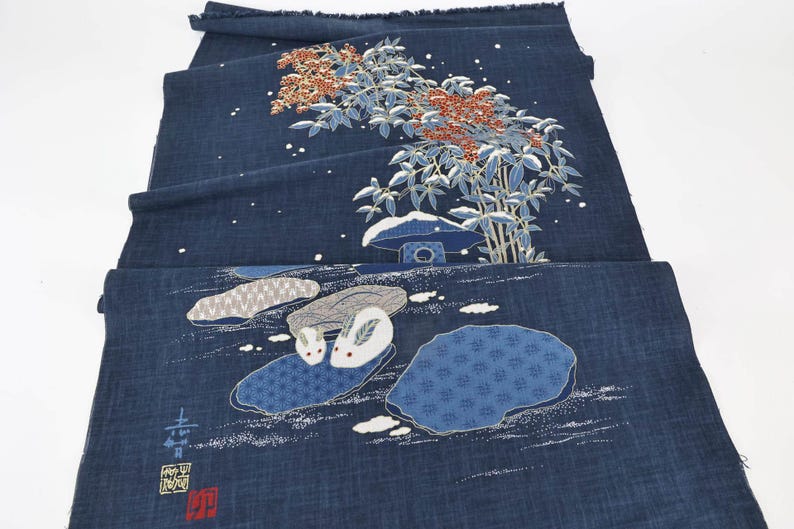 May include: Indigo blue fabric with a Japanese-style design. The fabric features a detailed illustration of a tree with red berries, a small structure, and two rabbits. The design also includes white accents and text.