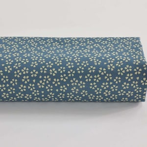 May include: A rolled length of blue fabric, patterned with small, cream-coloured floral motifs. The fabric is neatly rolled, displaying the detailed floral design. The background is a plain white surface.