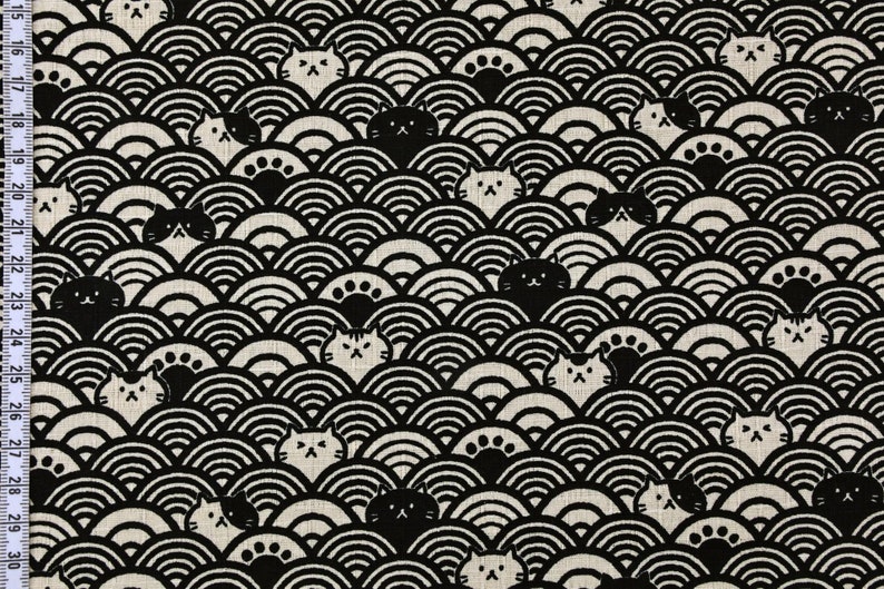 Op de afbeelding: Zwart-witte stof met een herhalend patroon van katten en golven. De katten zijn gestileerd en hebben een eenvoudig ontwerp. De golven zijn in een traditioneel Japans patroon.