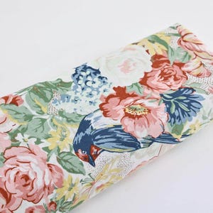 Peut inclure: Un tissu blanc avec un imprimé floral composé de fleurs roses, rouges et bleues, de feuilles vertes et d'un oiseau bleu.
