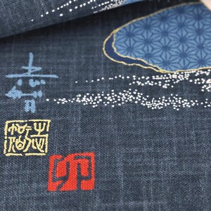 May include: Close-up of a dark blue fabric with Japanese-style designs. The fabric features blue and gold floral patterns, white dotted accents, and Japanese characters in blue, yellow, and red.