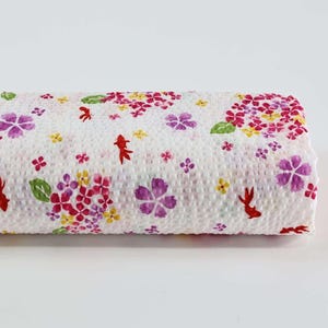 Könnte beinhalten: Eine Rolle weißer Papiertücher mit floralem Muster. Das Design umfasst rosa, lila und gelbe Blumen, grüne Blätter und rote Fische. Die Papiertücher sind aufgerollt.