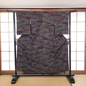 May include: A patterned kimono in shades of brown, burgundy, and gray is displayed on a black metal rack. The fabric features an abstract geometric design. The kimono is hanging in front of a traditional Japanese sliding door.