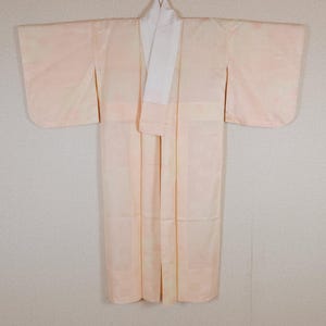 Peut inclure: Un kimono rose pâle avec un col blanc. Ce vêtement traditionnel japonais présente de longues manches et un design enveloppant. Le tissu a un motif subtil et le kimono est présenté sur un fond neutre.