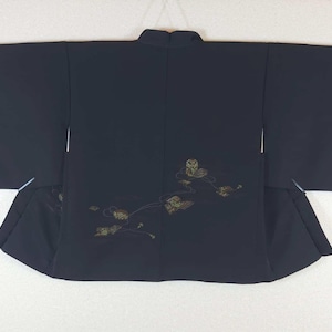 Peut inclure: Kimono noir avec de larges manches et un col mandarin. Le dos du kimono présente un motif floral brodé en or et vert. Le vêtement est fait d'un tissu sombre et lisse et est présenté à plat.