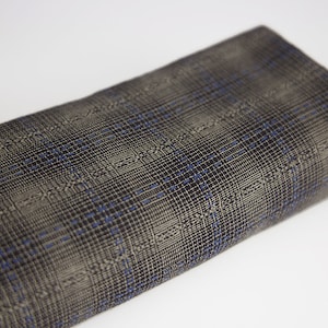 Könnte beinhalten: Nahaufnahme eines grauen und schwarzen karierten Stoffes mit einem dezenten blauen Muster. Der Stoff ist gefaltet und hat eine strukturierte Oberfläche.