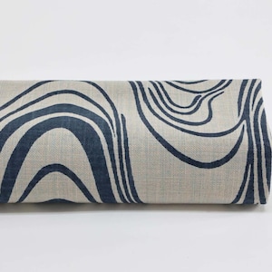Peut inclure: Tissu roulé avec un fond beige et un motif abstrait de vagues bleu marine. Le tissu est enroulé, mettant en valeur les lignes répétitives du motif. La texture du tissu est visible, suggérant une fibre naturelle.