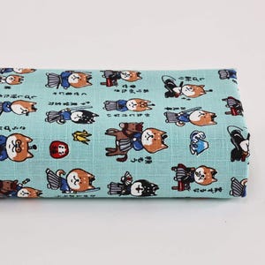 Peut inclure: Tissu bleu clair plié avec un motif répété de chiens Shiba Inu de dessin animé dans diverses poses et tenues. Les chiens sont dans des tons de marron, noir et blanc, avec du texte japonais. Le tissu est probablement en coton ou en lin.