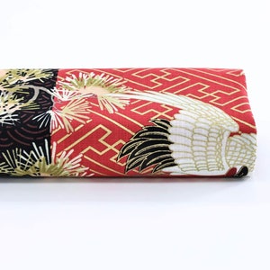 May include: Red fabric with a gold and white crane design. The crane's wings are spread out and the fabric has a geometric pattern in the background.